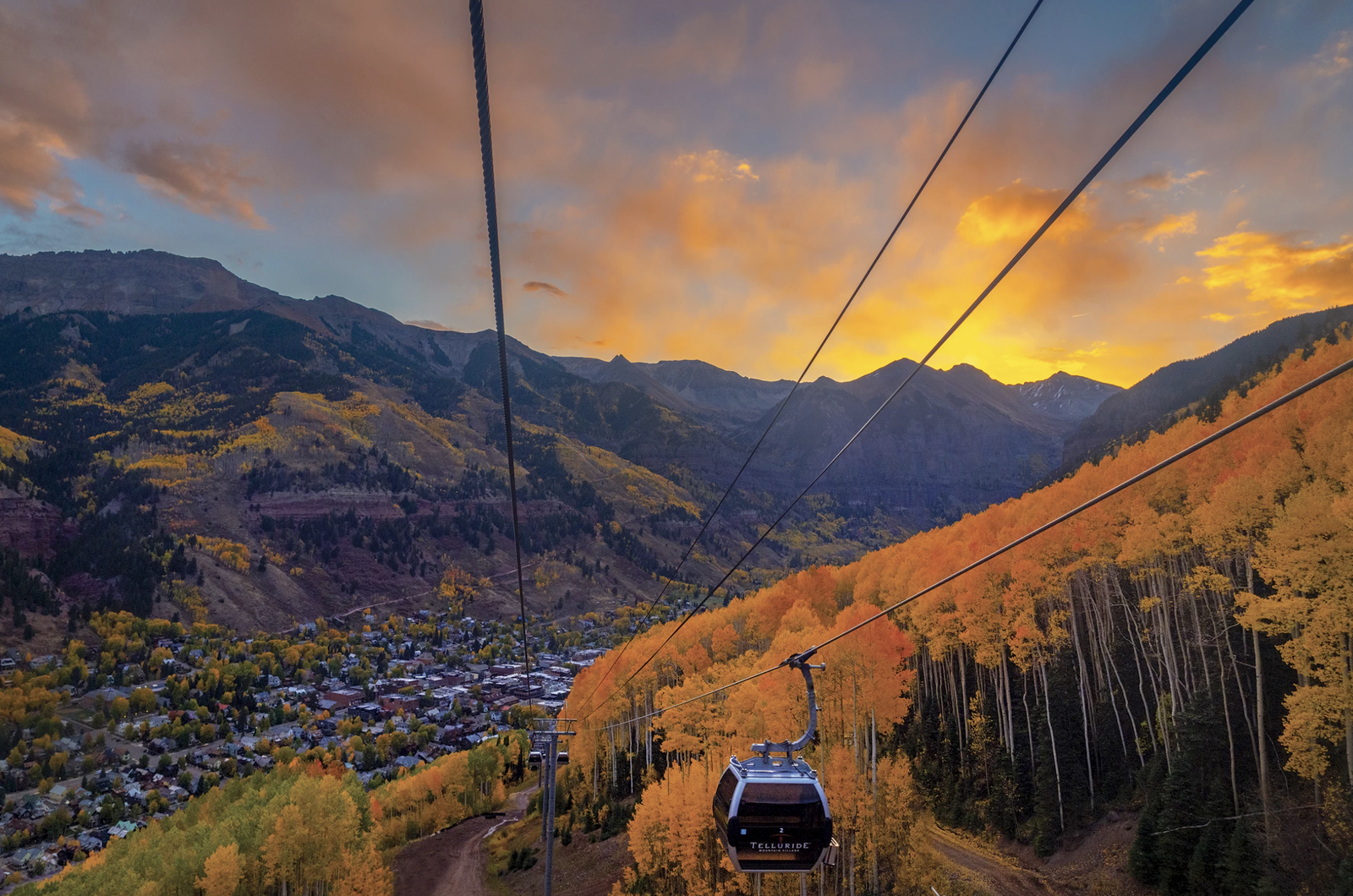 A gondola above an autumn valley town at sunset, golden aspens on the slopes.