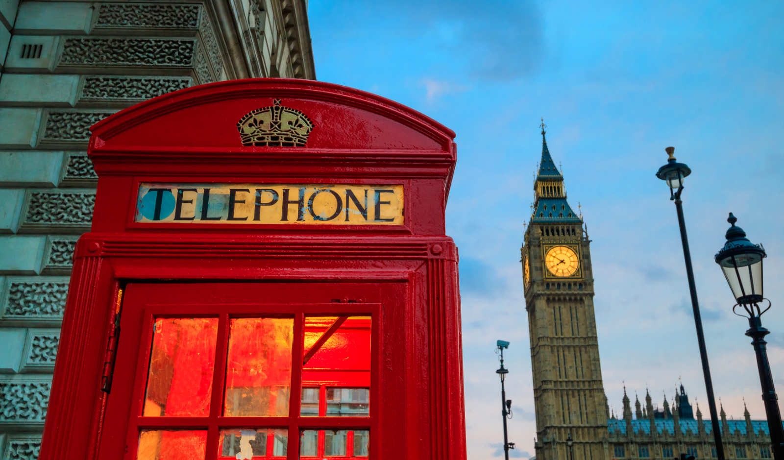 A red British telephone box in London, with Big Ben's clock tower behind it at dusk.