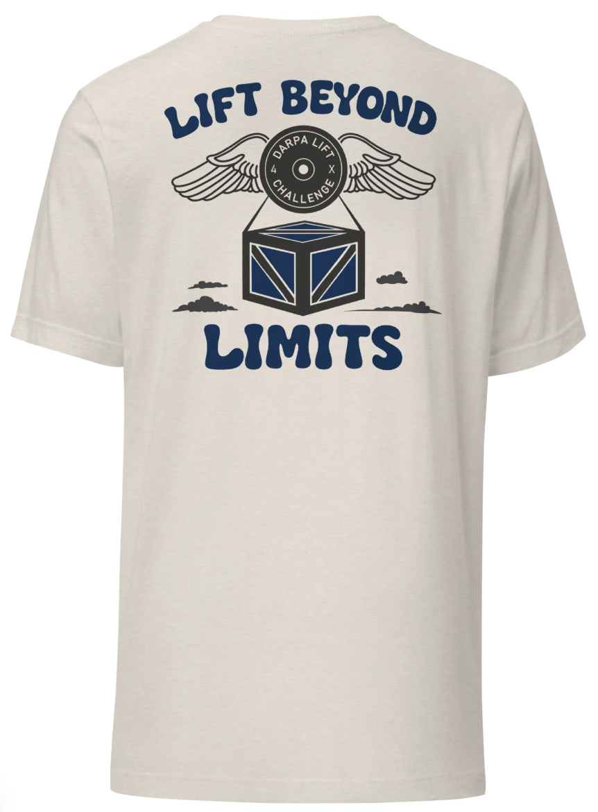 The back of a cream T-shirt that reads Lift Beyond Limits, with the winged DARPA Lift Challenge weight plate carrying a crate among clouds.